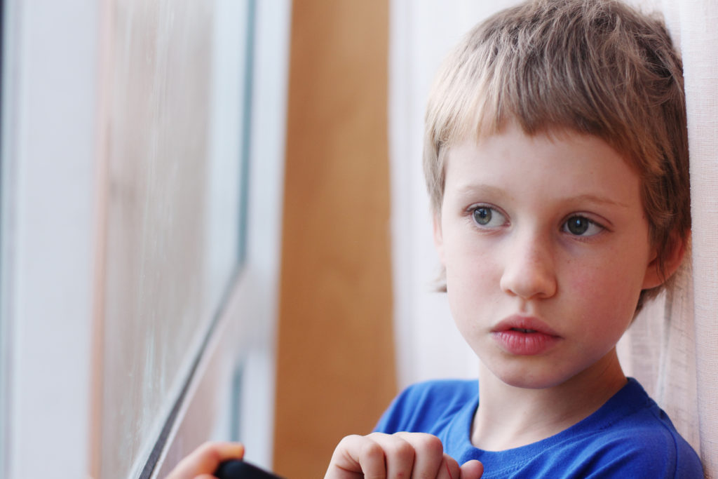 Cute 6 years old boy looking through the window